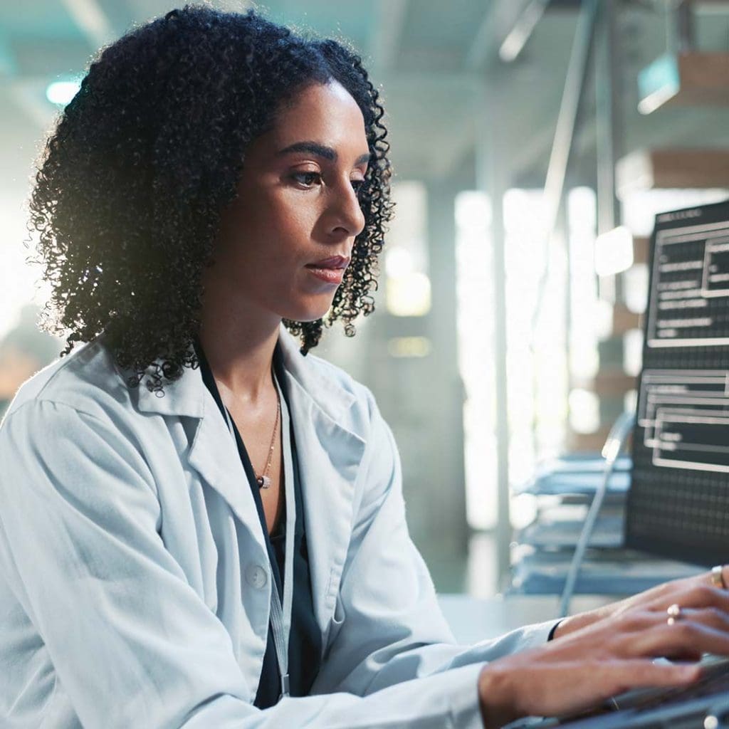 Woman in a laboratory holding a tablet, with a laptop computer screen visible nearby.